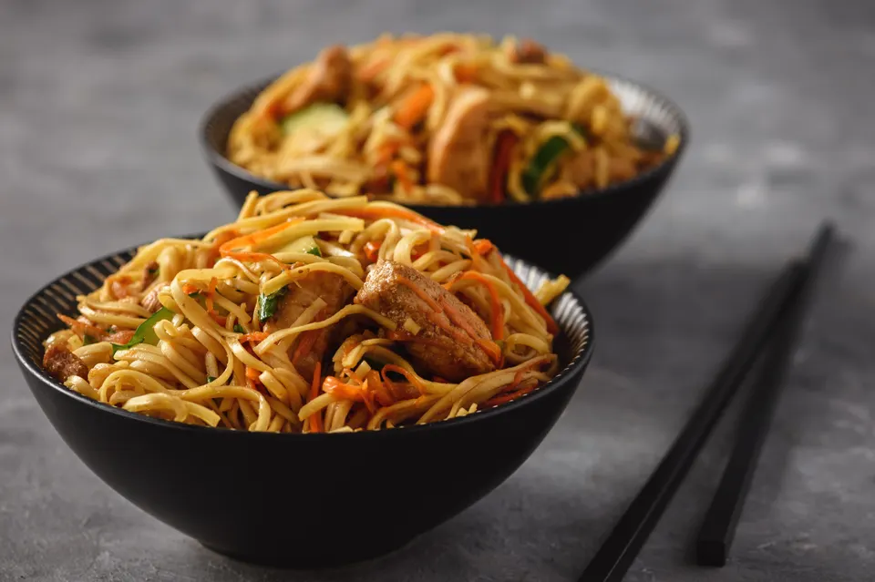 Two black bowls of egg noodles with chicken and chopsticks